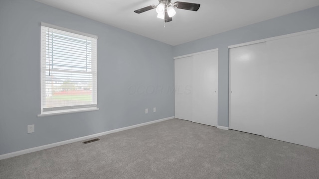 unfurnished bedroom with carpet, visible vents, baseboards, two closets, and ceiling fan