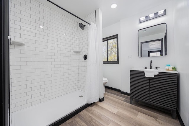 full bathroom with a tile shower, toilet, wood finished floors, and baseboards