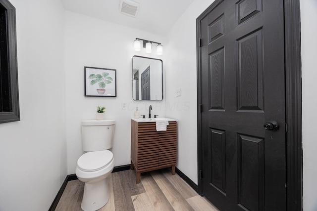 bathroom with vanity, baseboards, toilet, visible vents, and wood finished floors