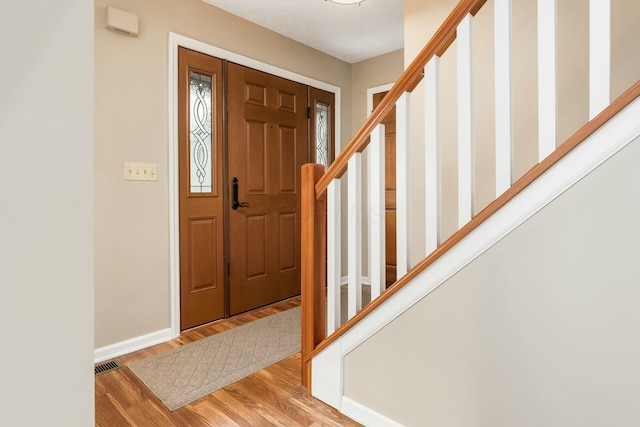 entryway featuring stairway, baseboards, wood finished floors, and visible vents