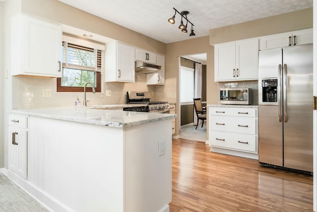 kitchen featuring a peninsula, a sink, white cabinetry, under cabinet range hood, and appliances with stainless steel finishes