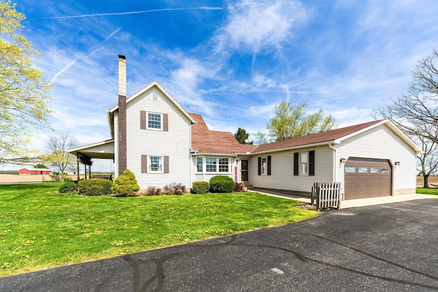 traditional-style home with a front yard, an attached garage, a chimney, and aphalt driveway