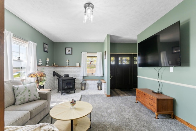 carpeted living room featuring wood finished floors, baseboards, a textured ceiling, and a wood stove