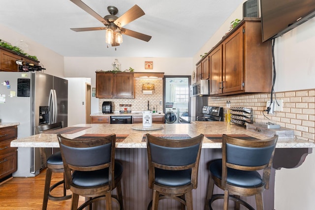 kitchen with stainless steel appliances, backsplash, a ceiling fan, separate washer and dryer, and a peninsula