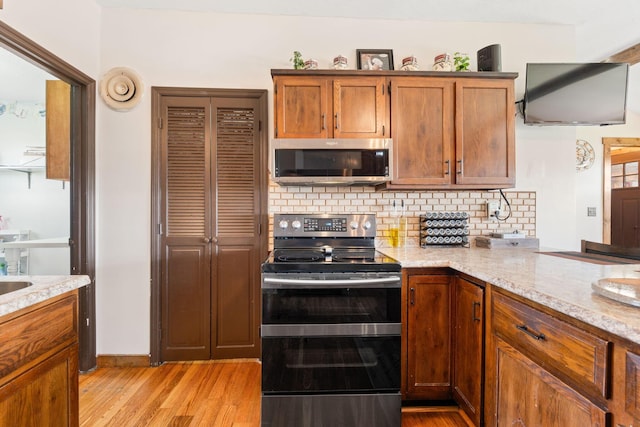 kitchen featuring brown cabinetry, backsplash, stainless steel appliances, and light wood-style floors