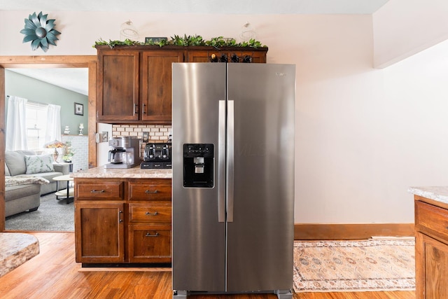 kitchen with backsplash, light wood-style floors, stainless steel refrigerator with ice dispenser, and light stone counters