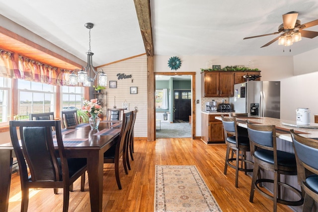dining space featuring light wood-type flooring, vaulted ceiling with beams, ceiling fan, and wood walls