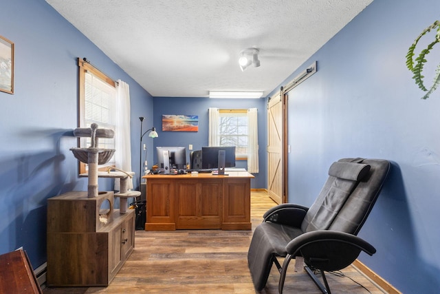 office space with baseboard heating, a barn door, a textured ceiling, and light wood-style flooring
