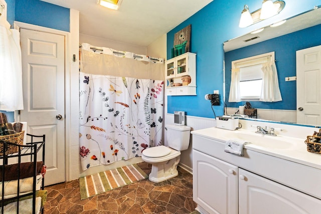 full bath featuring visible vents, toilet, vanity, and wainscoting