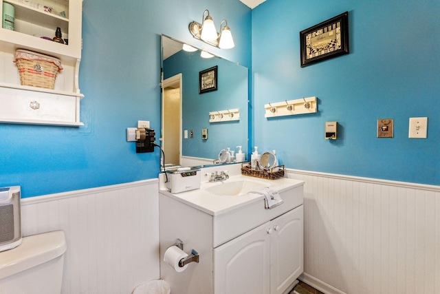 half bath featuring wainscoting, toilet, wood walls, and vanity