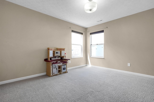 carpeted empty room with baseboards, a textured ceiling, and visible vents