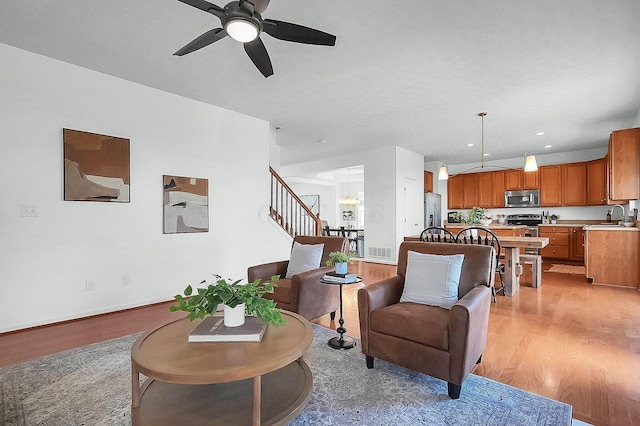living room featuring visible vents, baseboards, light wood-style floors, stairway, and ceiling fan