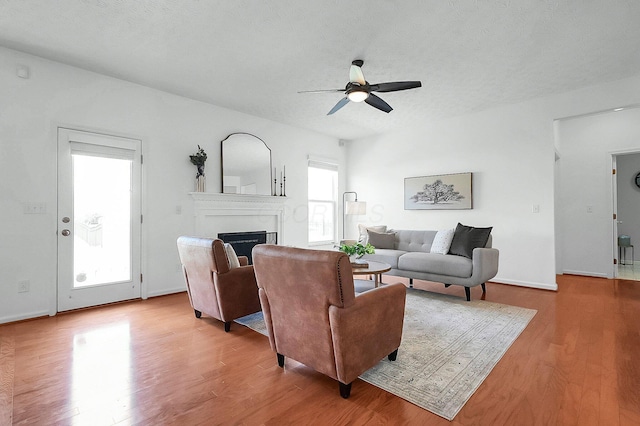 living room with a ceiling fan, wood finished floors, a textured ceiling, and a fireplace