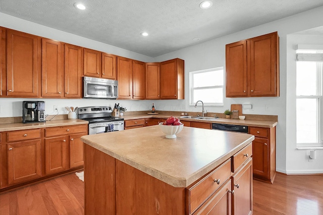 kitchen with a sink, brown cabinets, light wood finished floors, appliances with stainless steel finishes, and recessed lighting