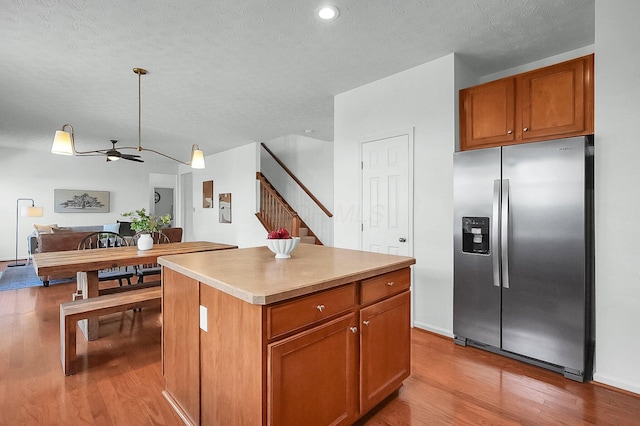 kitchen with brown cabinets, stainless steel fridge with ice dispenser, wood finished floors, a ceiling fan, and a kitchen island