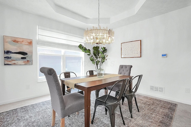 dining space with a tray ceiling, visible vents, carpet floors, baseboards, and a chandelier