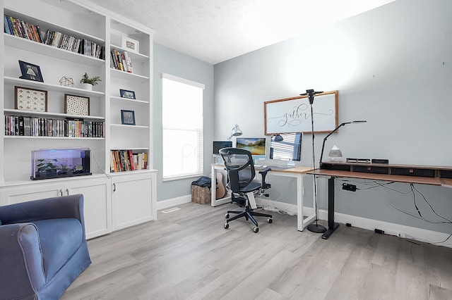 office area with light wood-type flooring, a textured ceiling, built in features, and baseboards