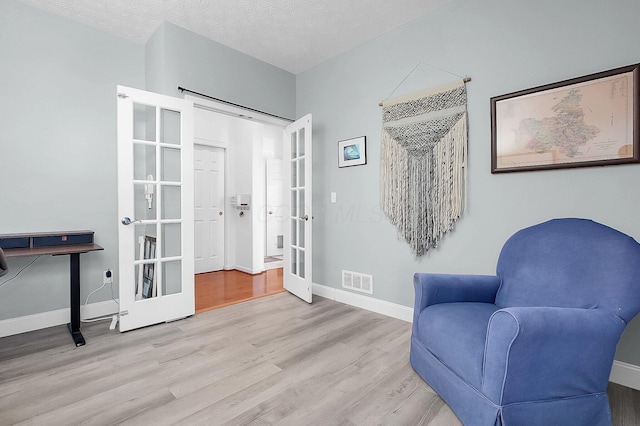 sitting room featuring wood finished floors, visible vents, french doors, baseboards, and a textured ceiling