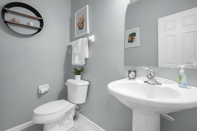 half bath with baseboards, tile patterned flooring, a sink, and toilet