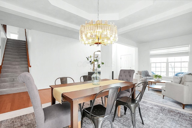 dining space featuring light wood finished floors, a tray ceiling, an inviting chandelier, and stairs