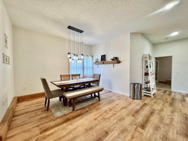 dining area with light wood-style flooring, a textured ceiling, baseboards, and a notable chandelier