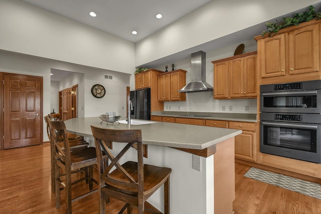 12372 Brook Forest Cir NW, Pickerington, OH 43147 - kitchen featuring wall chimney range hood, black appliances, a kitchen bar, and light wood finished floors
