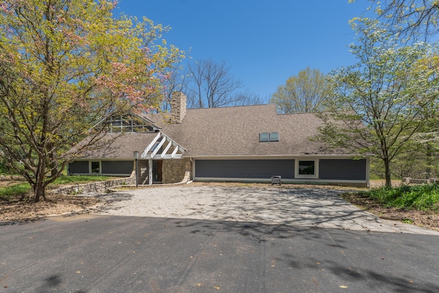 view of front of house with a garage, roof with shingles, driveway, and a chimney
