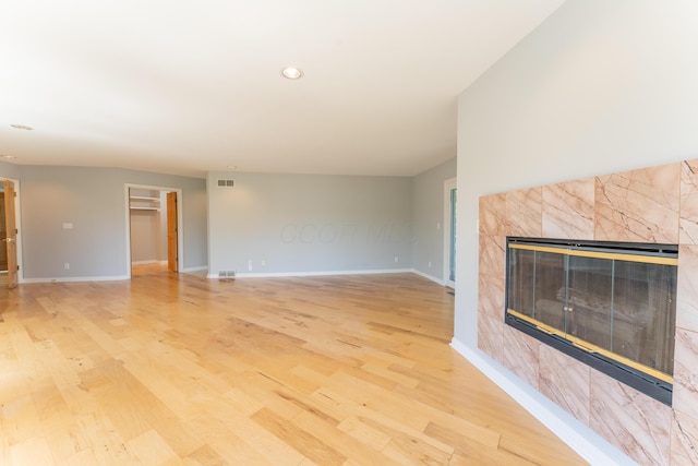 unfurnished living room with baseboards, light wood-style flooring, a tile fireplace, and visible vents