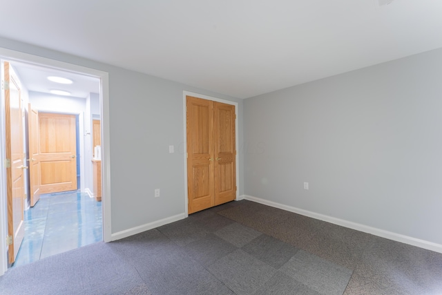 unfurnished bedroom with baseboards, a closet, and dark carpet