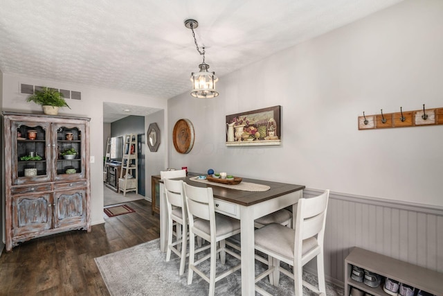 dining room with wood finished floors, visible vents, a wainscoted wall, and a notable chandelier
