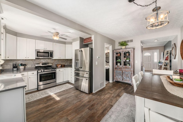 kitchen with white cabinets, dark wood-style flooring, tasteful backsplash, ceiling fan with notable chandelier, and appliances with stainless steel finishes