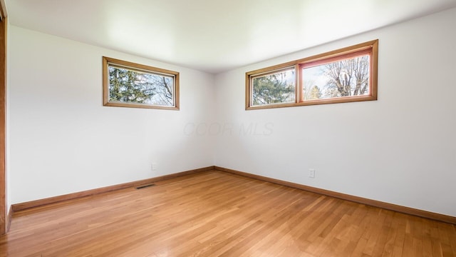spare room with plenty of natural light, light wood-style flooring, visible vents, and baseboards