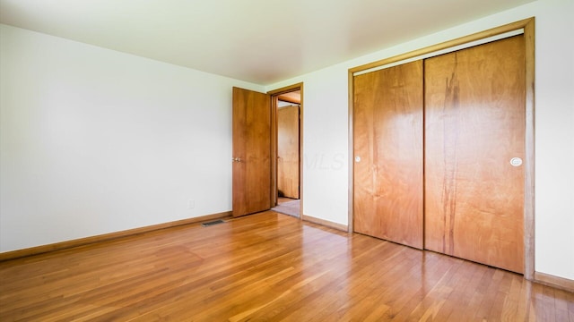 unfurnished bedroom featuring light wood-style floors, baseboards, visible vents, and a closet