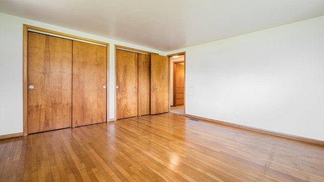 unfurnished bedroom with visible vents, light wood-style flooring, baseboards, and two closets