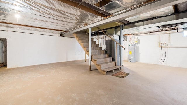 unfinished basement with stairway, water heater, and concrete block wall