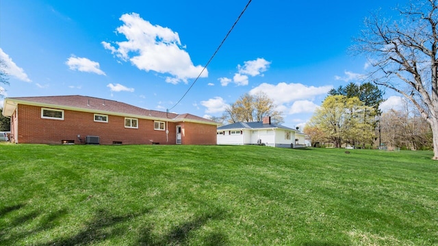 rear view of property with brick siding, a lawn, and central AC unit