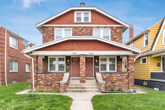 american foursquare style home with brick siding, a front lawn, and covered porch