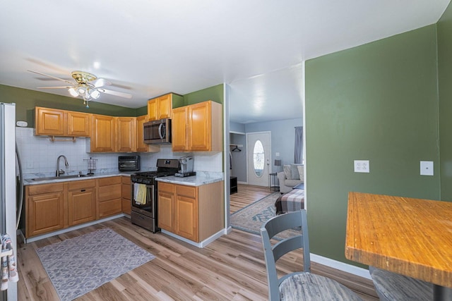 kitchen featuring light wood finished floors, stainless steel appliances, a sink, tasteful backsplash, and light countertops