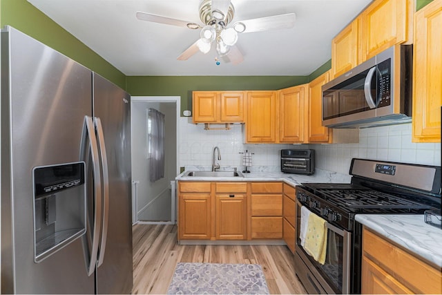 kitchen with stainless steel appliances, backsplash, a sink, light wood-type flooring, and ceiling fan