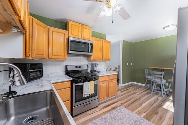 kitchen featuring light wood finished floors, a ceiling fan, a sink, tasteful backsplash, and appliances with stainless steel finishes