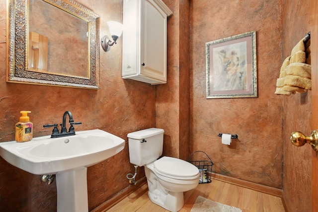 bathroom with baseboards, wood finished floors, a sink, and toilet
