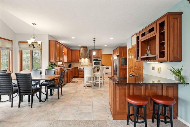 kitchen with brown cabinetry, a peninsula, an inviting chandelier, and appliances with stainless steel finishes