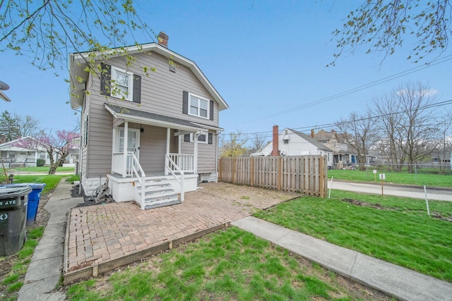 view of front of property with a porch, a front lawn, a chimney, and fence