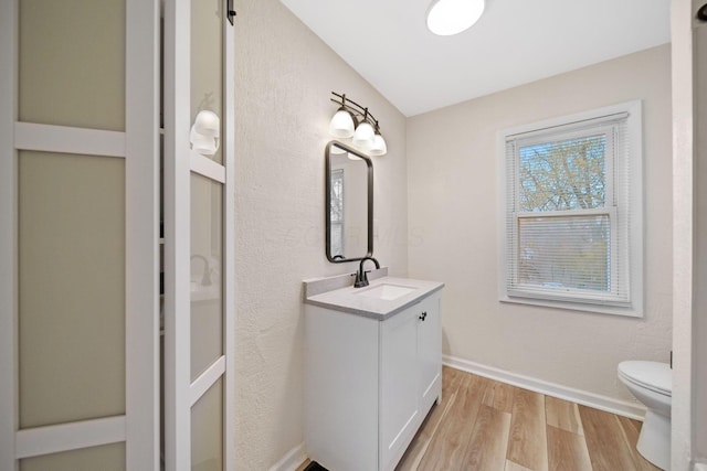 bathroom with baseboards, wood finished floors, vanity, and toilet