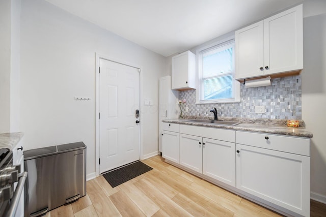 kitchen featuring stove, a sink, light wood-style flooring, tasteful backsplash, and white cabinetry