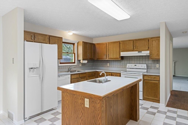 kitchen featuring white appliances, under cabinet range hood, light floors, a sink, and a textured ceiling