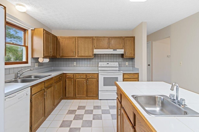 kitchen with white appliances, under cabinet range hood, a sink, a textured ceiling, and brown cabinetry