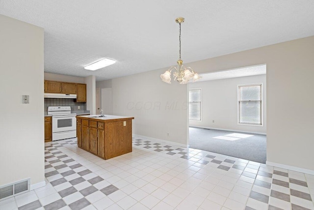 kitchen with electric range, under cabinet range hood, open floor plan, a sink, and brown cabinetry