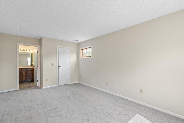 unfurnished bedroom featuring light carpet, baseboards, a textured ceiling, and ensuite bath