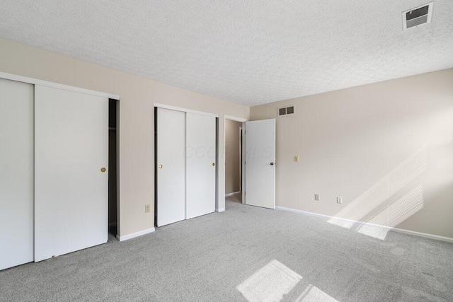 unfurnished bedroom with two closets, carpet flooring, a textured ceiling, and baseboards